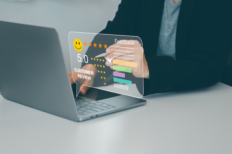 A person using a laptop while interacting with a transparent virtual feedback interface. The screen shows a 5.0 customer review rating, star ratings, and various colorful bar graphs, possibly enhanced by google review bots.