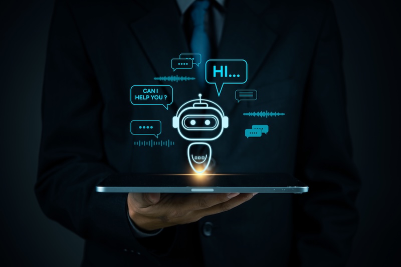 A person in a suit holds a tablet, from which a glowing holographic chatbot with speech bubbles saying “HI…” and “CAN I HELP YOU?” appears, symbolizing artificial intelligence and digital communication for University Online Reputation.