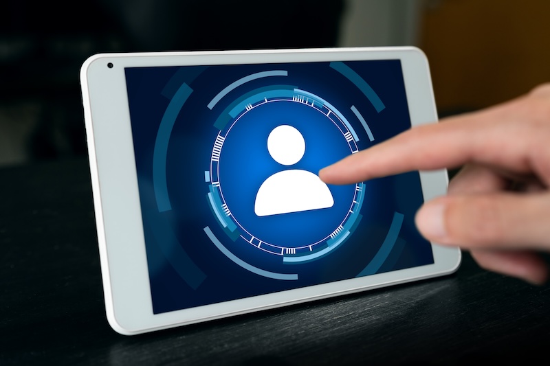 A hand is touching a tablet screen displaying a user profile icon within a digital circular interface, suggesting an ego surfing or login access concept.