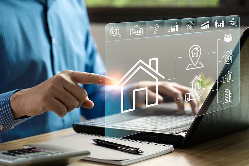 A person points at a virtual screen displaying real estate icons over a laptop, highlighting online property search and digital transactions—reminding us why Realtors need online reputation management today.