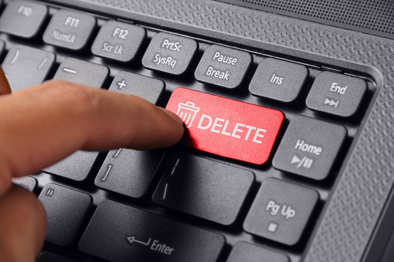 A close-up of a finger pressing a red "DELETE" key with a trash bin icon on a black computer keyboard, symbolizing the action to remove outdated content from Google search.